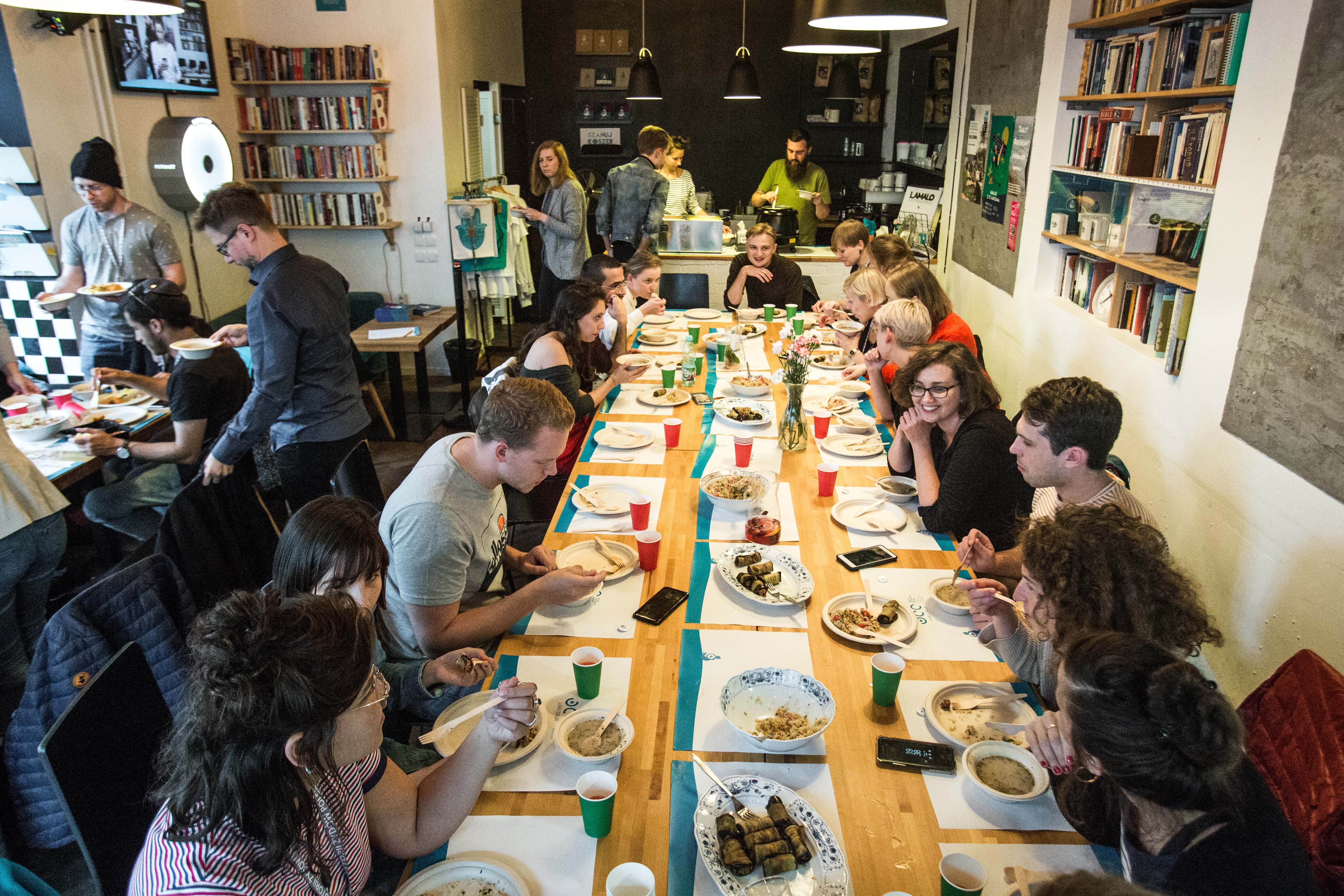Uczestnicy PIYE 2019 podczas uroczystej kolacji, na spotkaniu z Kuchnią Konfliktu i JCC. Wszyscy siedzą przy długim stole i jedzą posiłek.