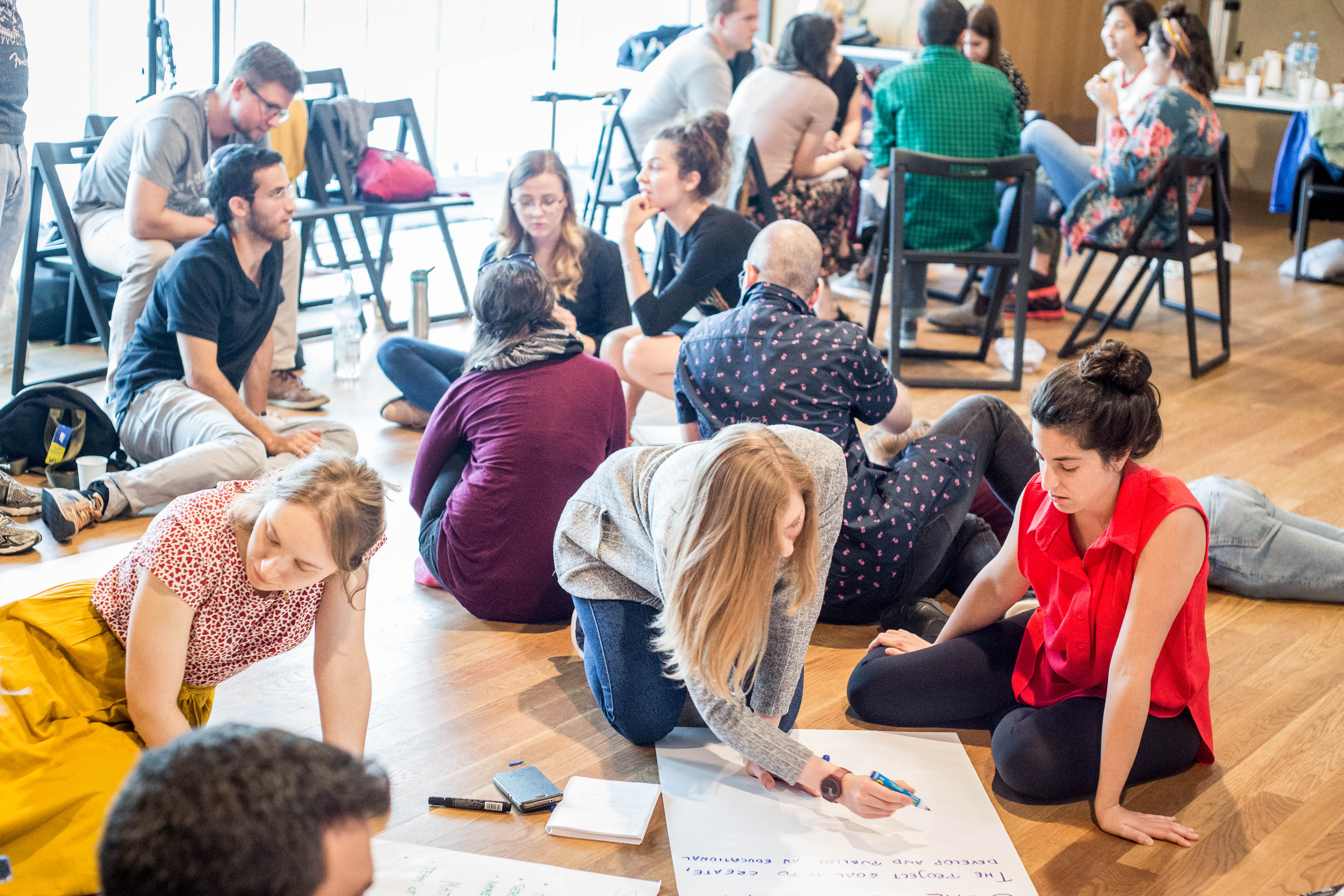 Uczestnicy PIYE 2019 siedzą na podłodze w sali podczas sesji warsztatowej, pracują przy dużych arkuszach papieru i notują