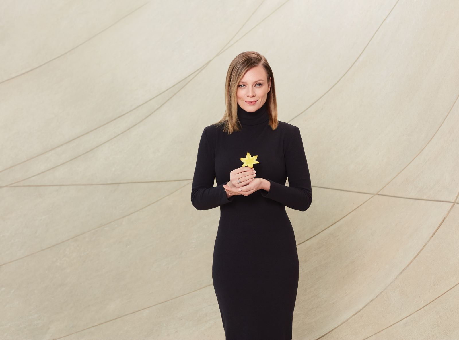 Magdalena Boczarska w czarnej sukni trzyma przed sobą w dłoni, na wysokości klatki piersiowej, żółty żonkil, symbol akcji