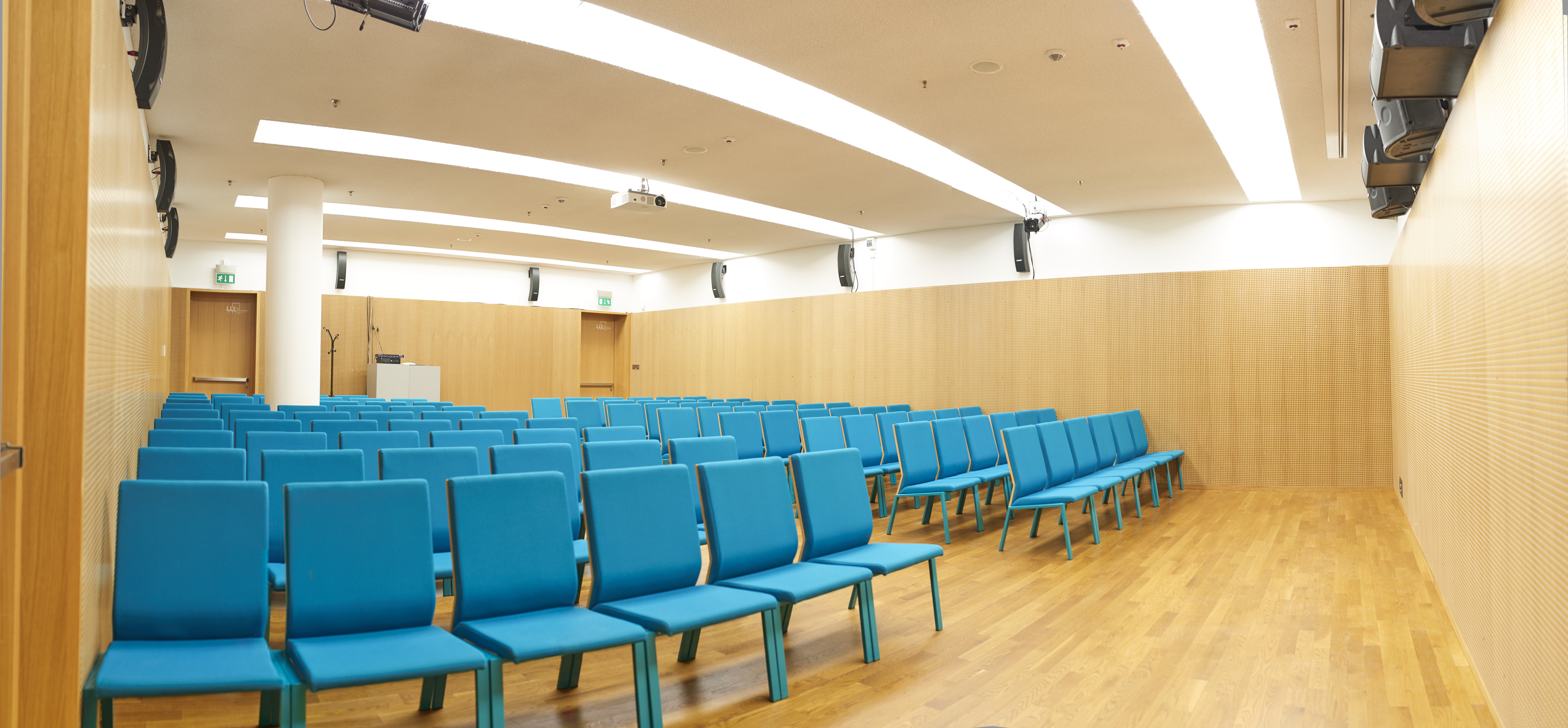 Sala konferencyjna A - widok na krzesła w kolorze niebiesko-zielonym. Krzesła stoją w rzędach. Sala jest pusta.