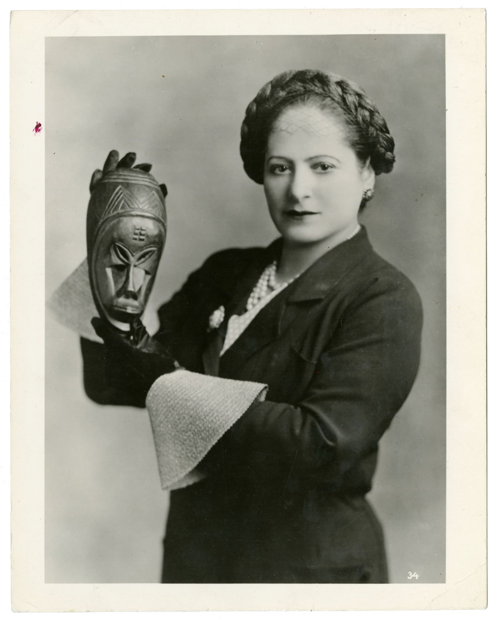 Helena Rubinstein. Kobieta z warkoczem uwiniętym wokół głowy. W dłoniach trzyma maskę.