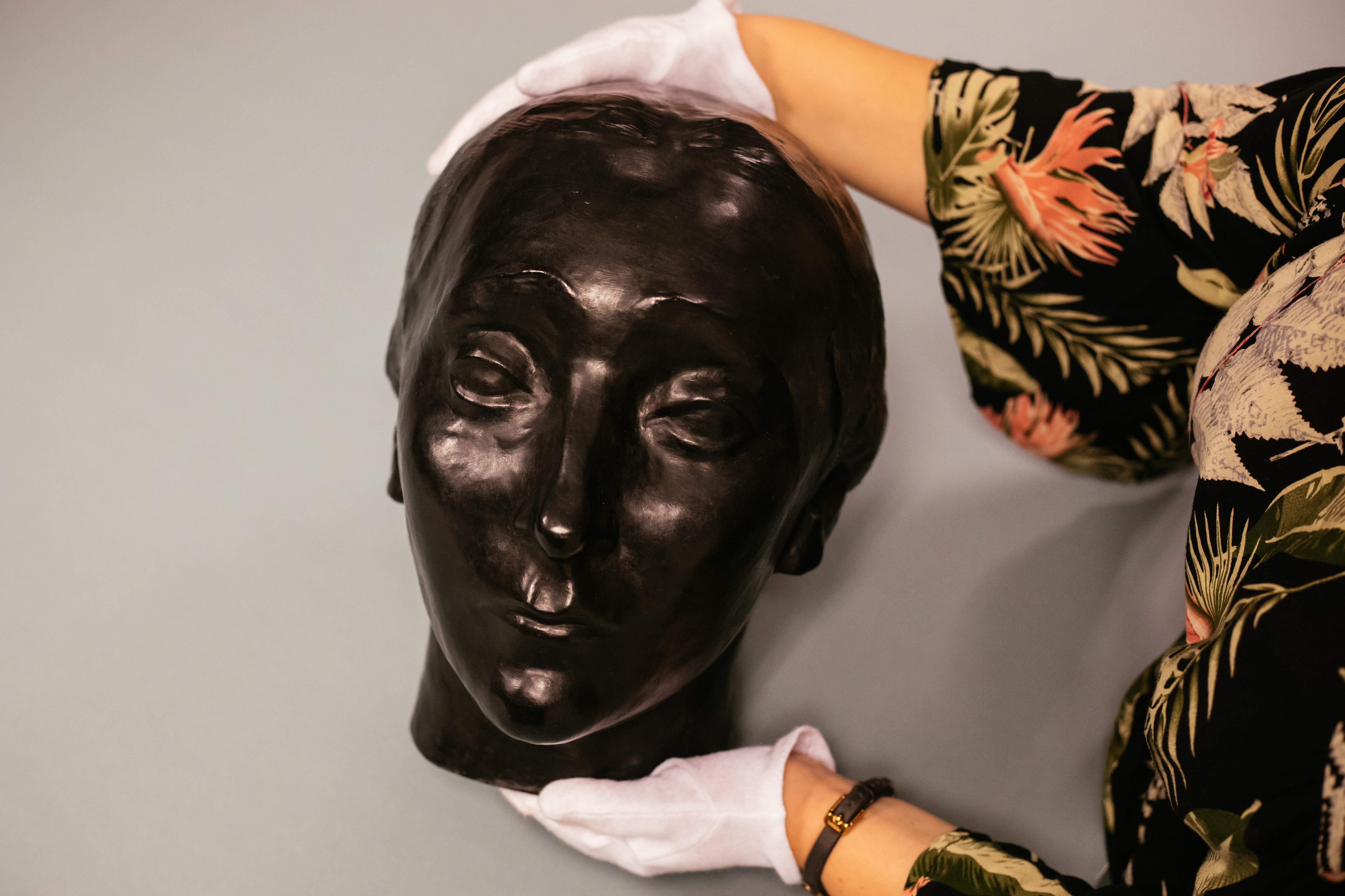 Kobieta w białych rękawiczkach trzyma rzeźbę z brązu przedstawiającą głowę Giny Szwarc.