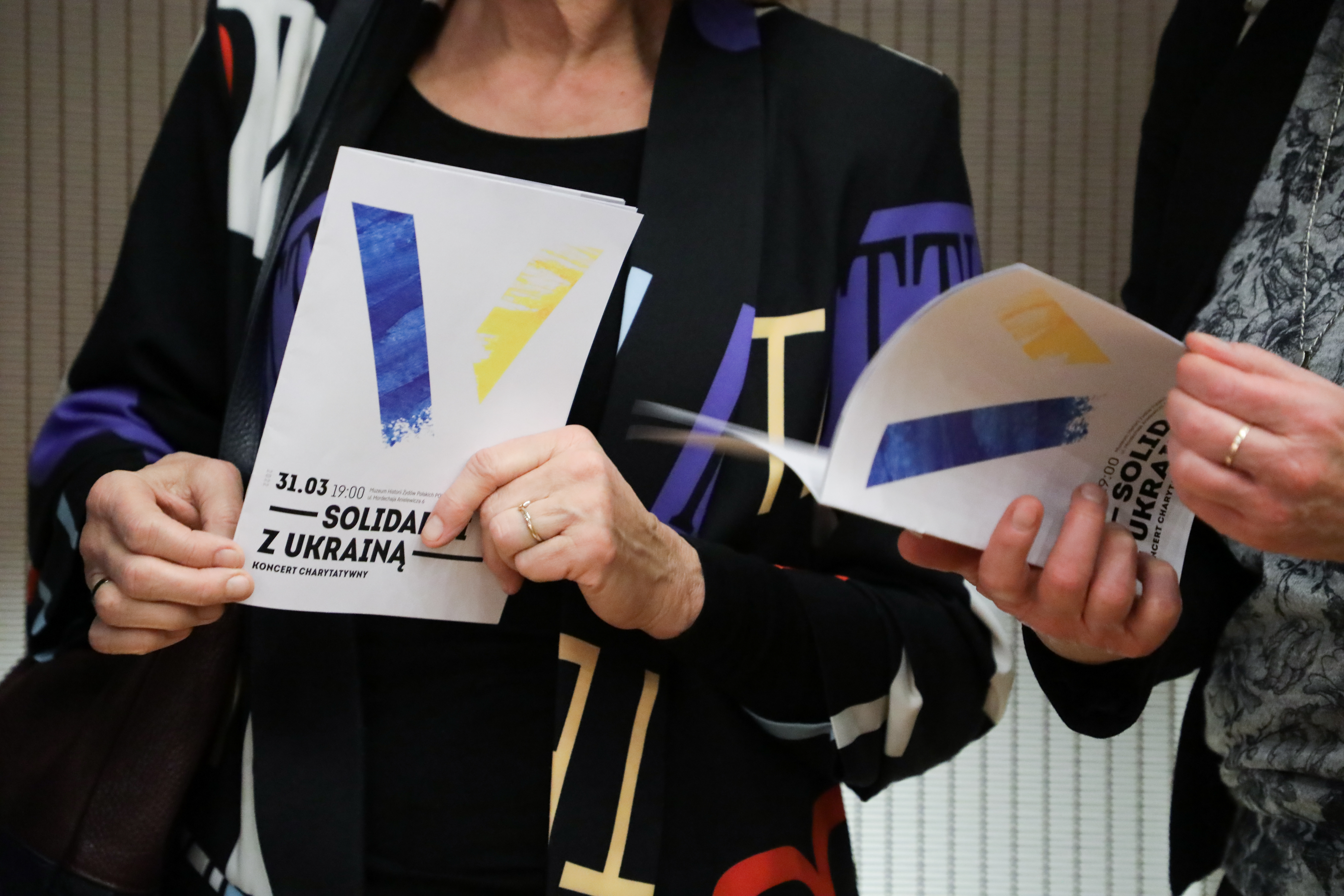 Dwie kobiety trzymają program koncertu "Solidarni z Ukrainą".