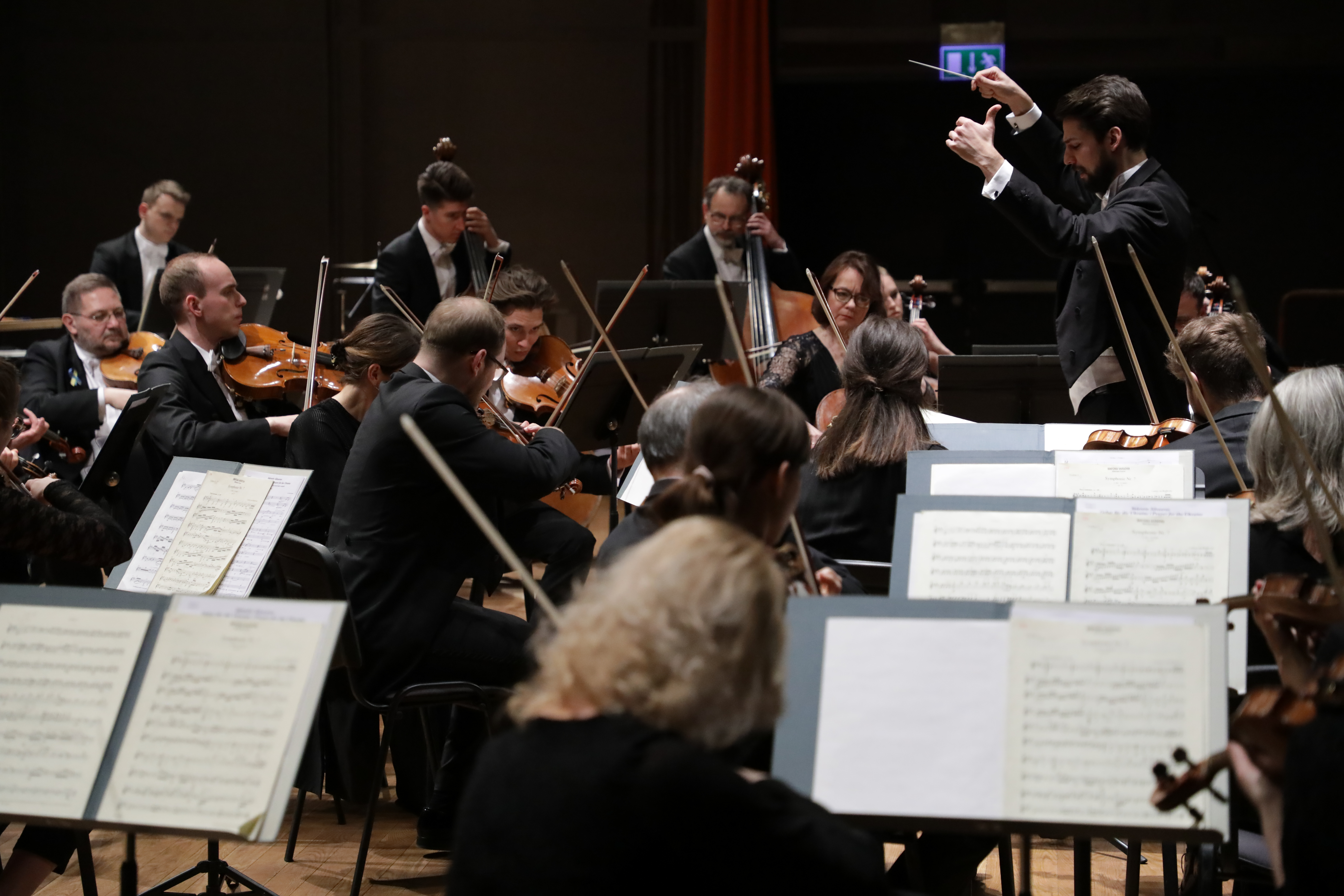 Muzycy Sinfonia Varsovia i pulpity na nuty. W tle dyrygent Yaroslav Shemet.