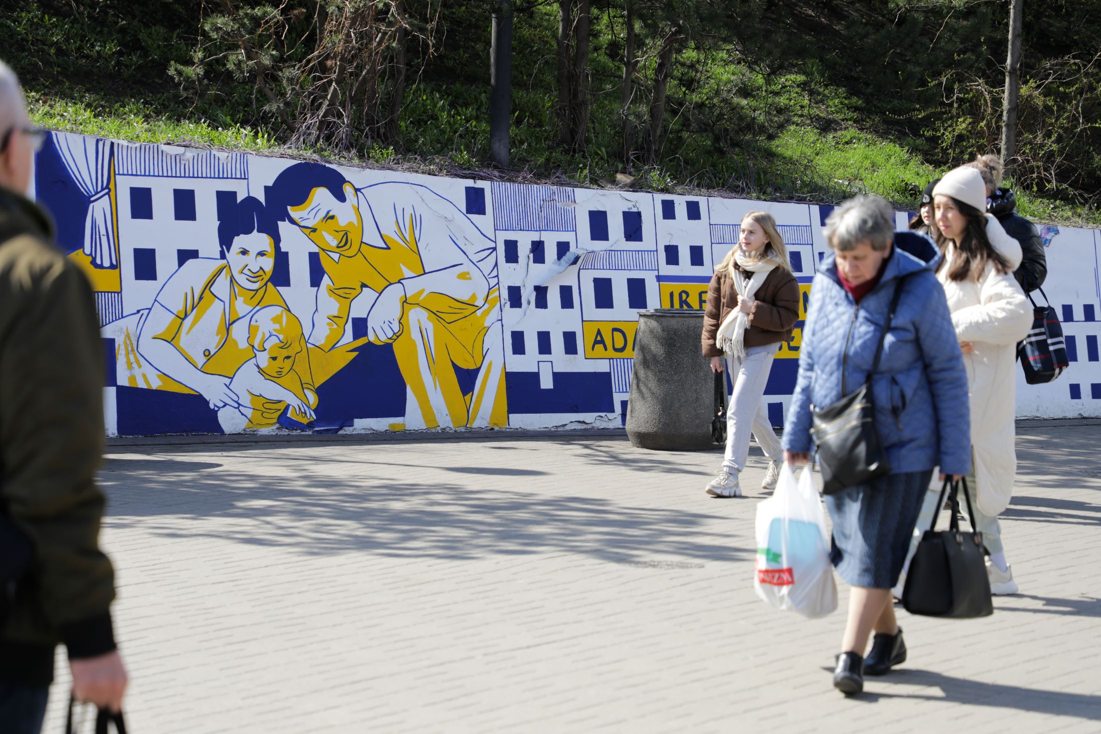 Ludzie na warszawskiej patelni, przy stacji metra Centrum. Na ścianie okalającej plac mural upamiętniający bohaterki i bohaterów powstania w getcie warszawskim.