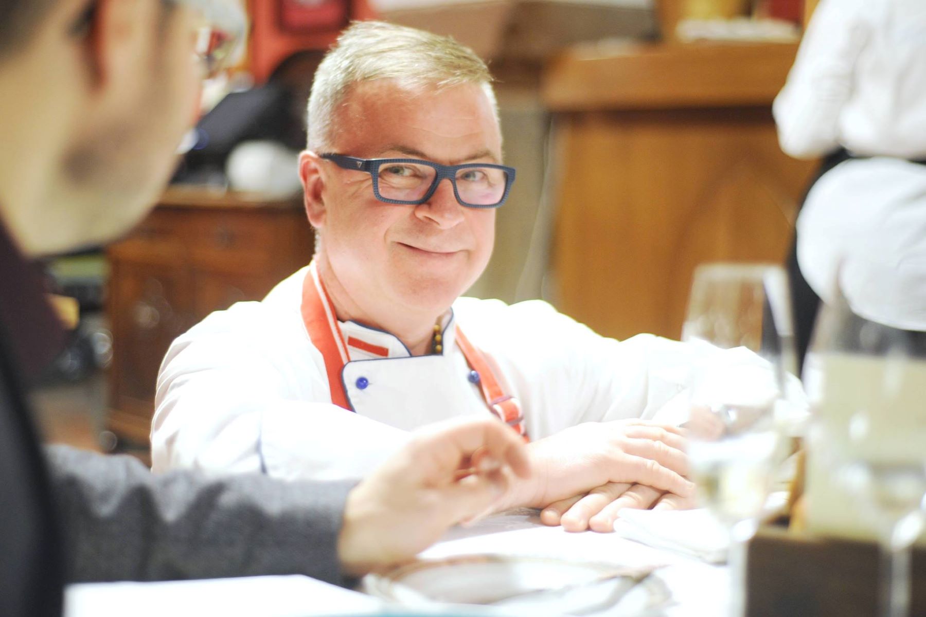 Szef kuchni Bogdan Gałązka siedzi przy stole, lekko się uśmiecha.