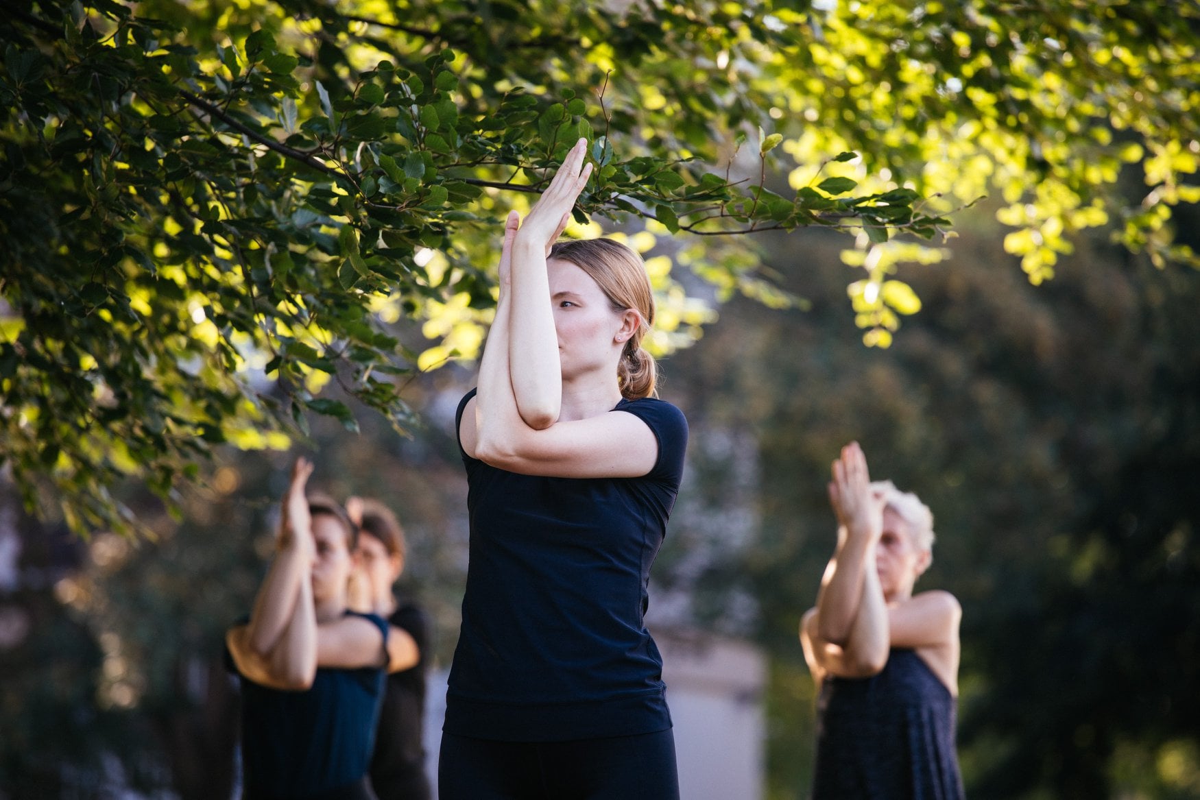 Cztery kobiety ćwiczą w parku podczas warsztatów ze świadomego ruchu. Przed sobą mają splecione ręce.