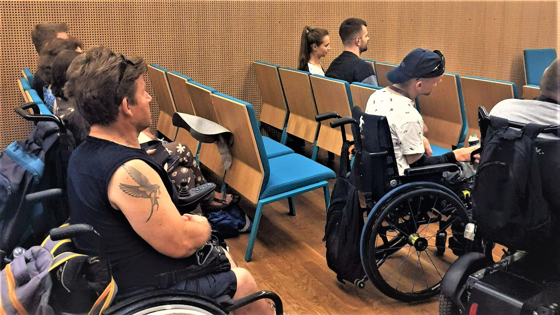 Grupa uczestników spotkania filmowego w Muzeum POLIN. Osoby z niepełnosprawnością ruchową siedzą w sali.