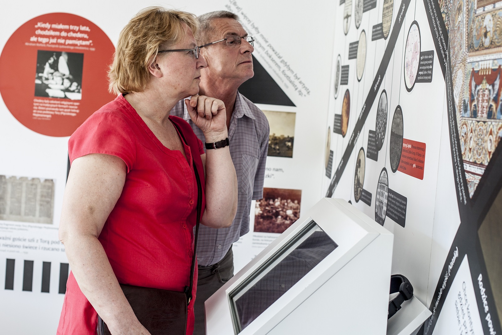 Kobieta i mężczyzna oglądają ekspozycję "Muzeum na kółkach" w Kielcach. Czytają opisy i oglądają zdjęcia umieszczone na ścianie.