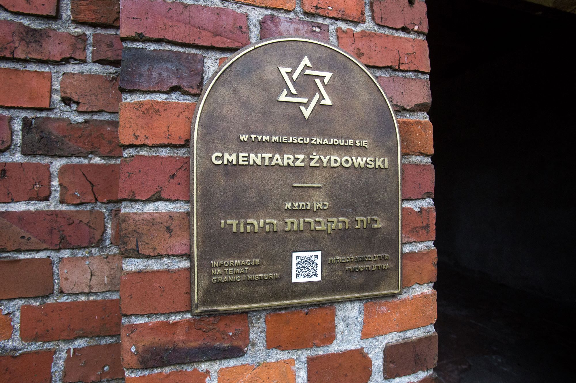 Tablica upamiętniająca cmentarz żydowski w Oleśnie, przytwierdzona do muru.