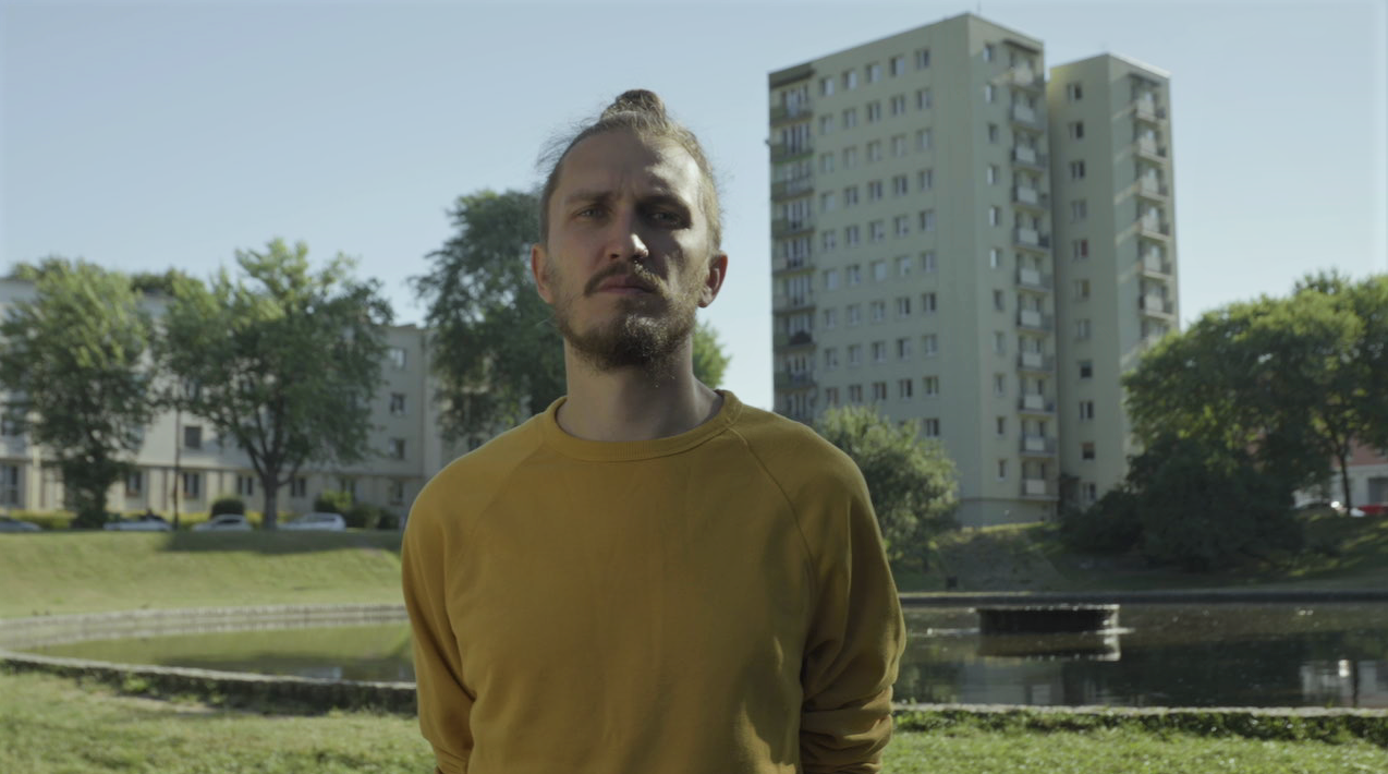 Łukasz Kamil Kamiński, reżyser, mężczyzna w żółtej bluzie stoi w parku.