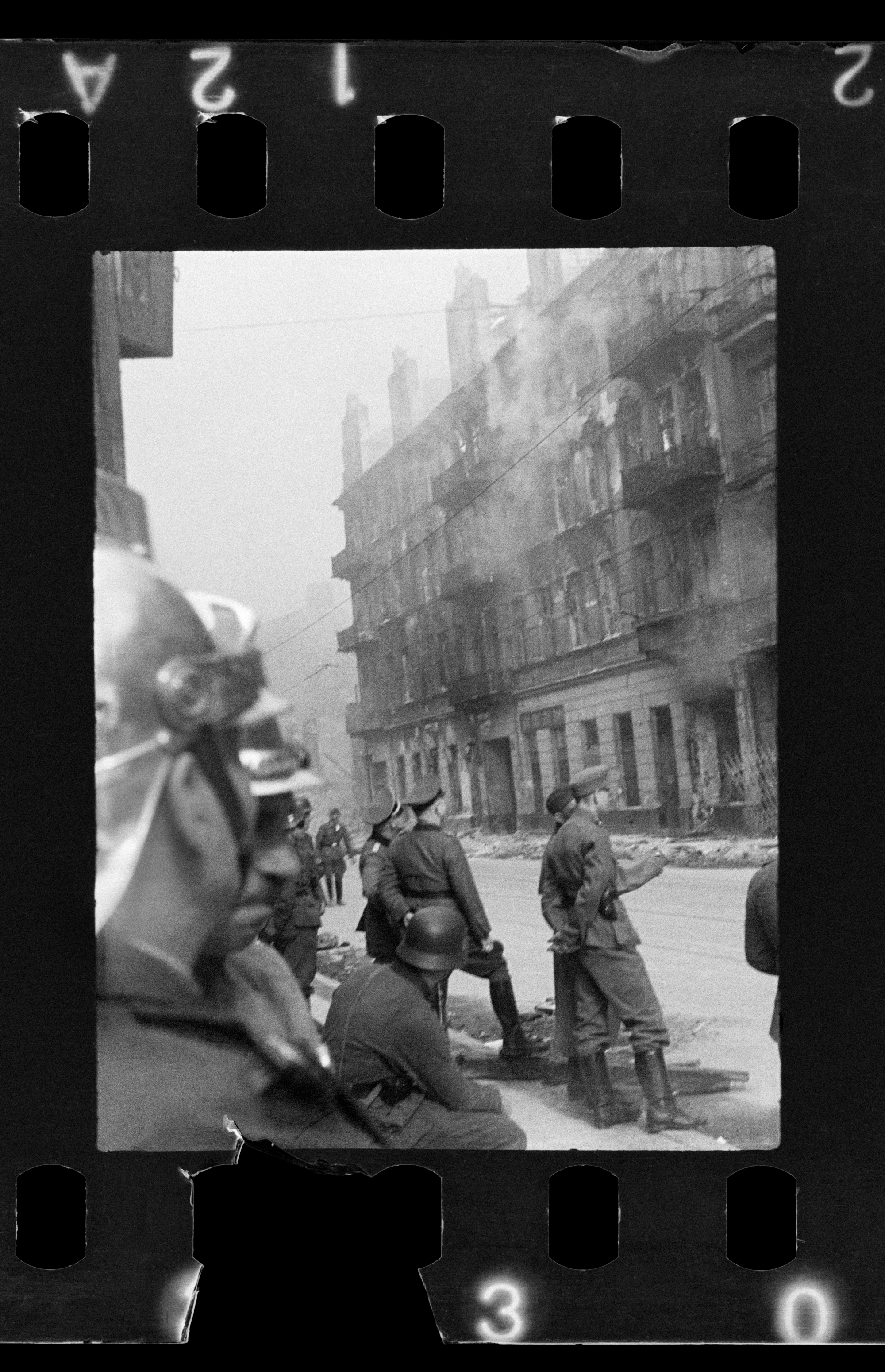 Ulica Nowolipie, 1943. Podpalona kamienica w dzielnicy żydowskiej. Wokół stoją Niemcy i strażak w hełmie.