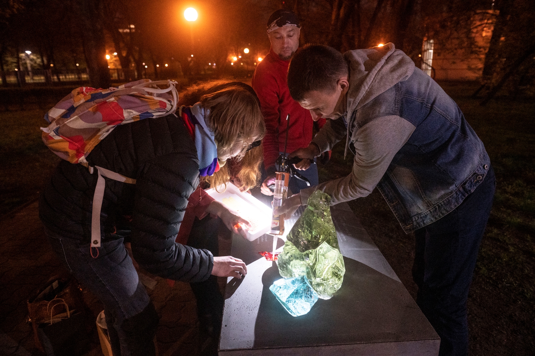 Natalia Romik i dwaj mężczyźni mocują kolorowe świecące kamienie na postumencie.