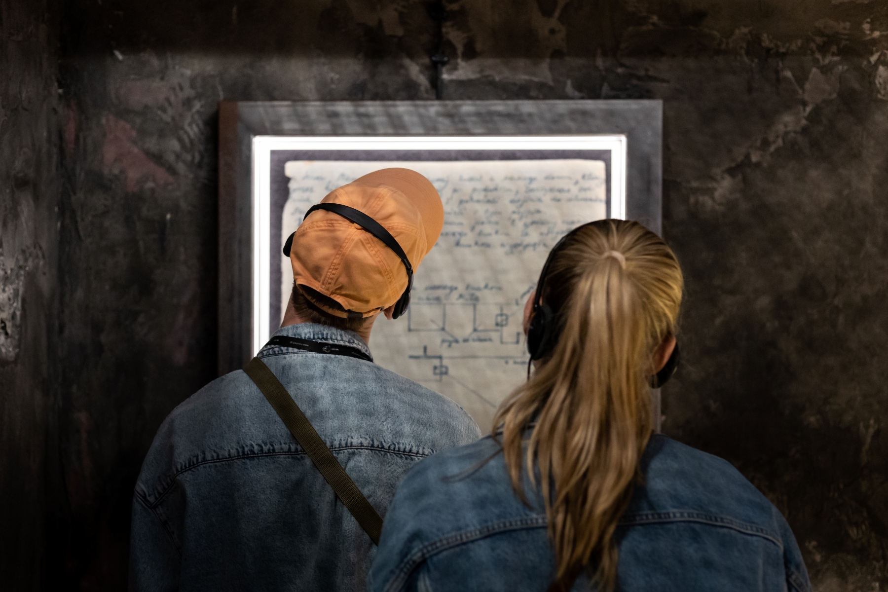 Chłopak i dziewczyna czytają fragment dziennika na wystawie "Wokół nas morze ognia". Stoją tyłem, ich twarze zwrócone w stronę ściany.