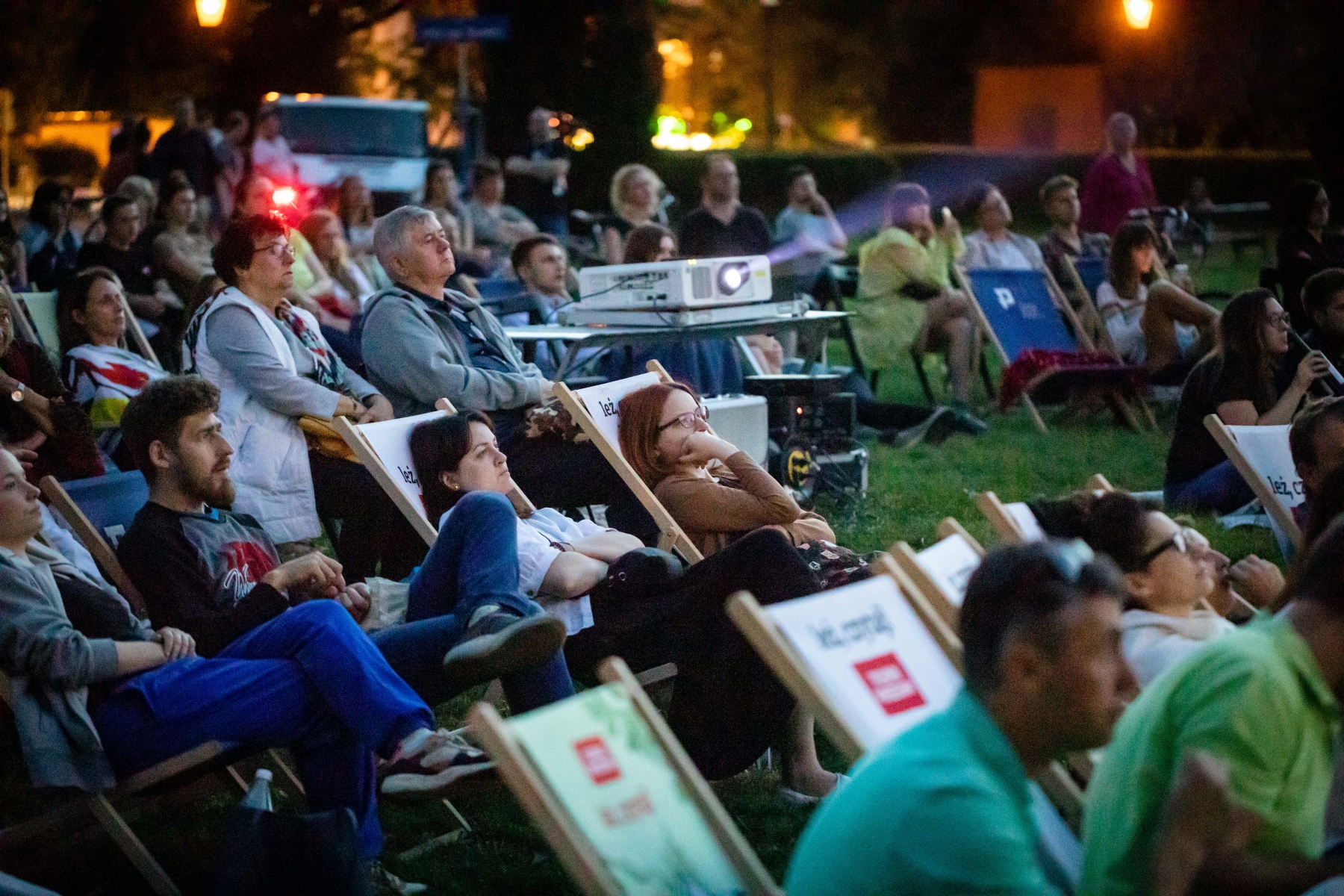 Widzowie kina letniego leżą na leżakach podczas seansu w ramach "POLIN na Łące".