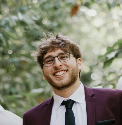 Uśmiechnięty rabin Shai Welfeld - młody chłopak w okularach i garniturze z krawatem.