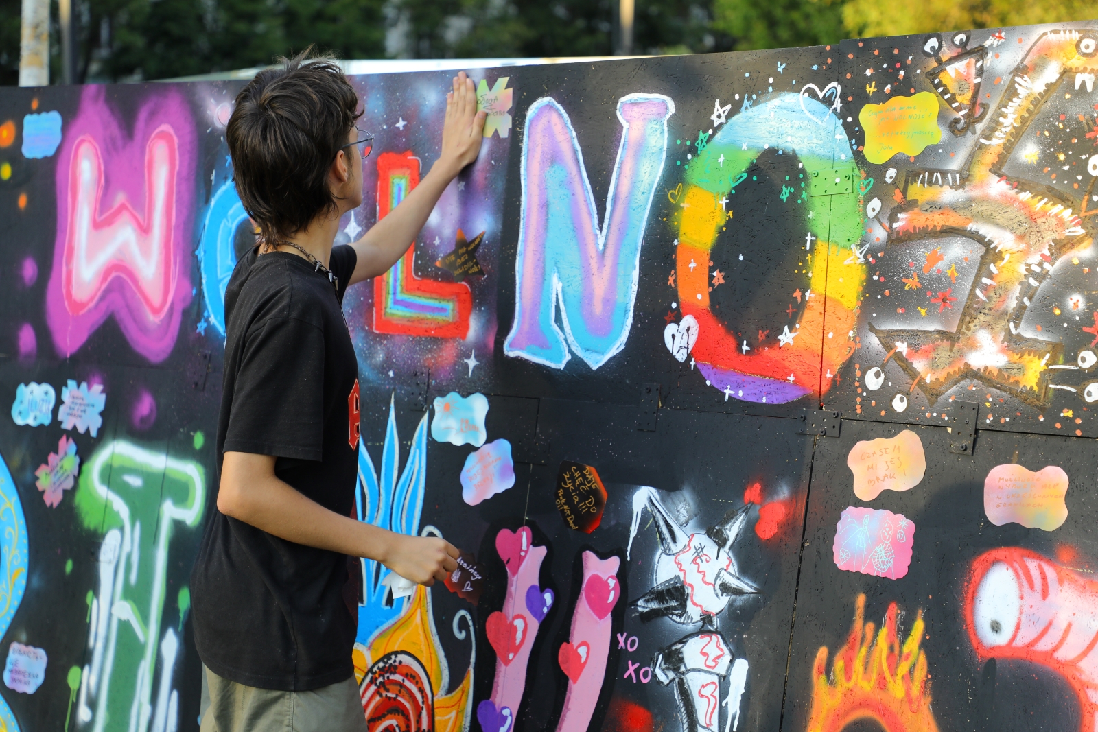 Chłopak trzyma dłoń na muralu z kolorowym napisem wolność.