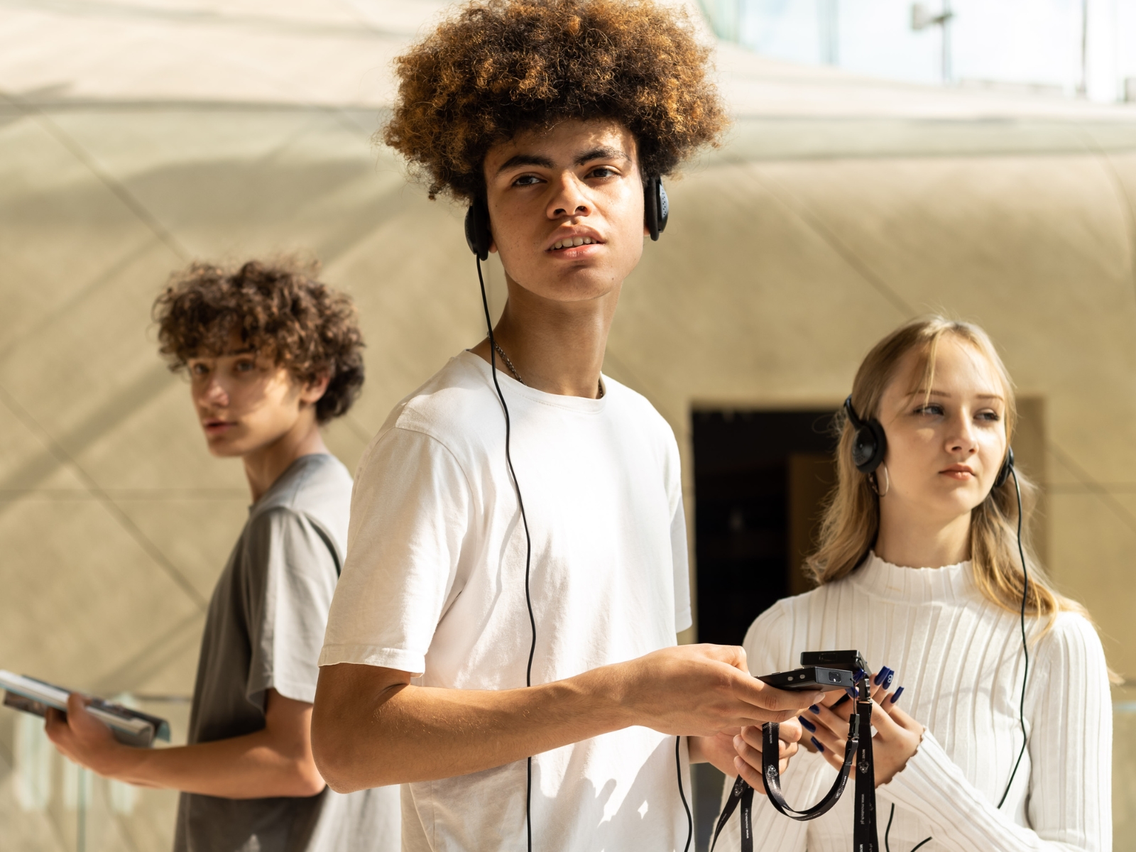 Troje nastolatków stoi w holu głównym ze słuchawkami na uszach