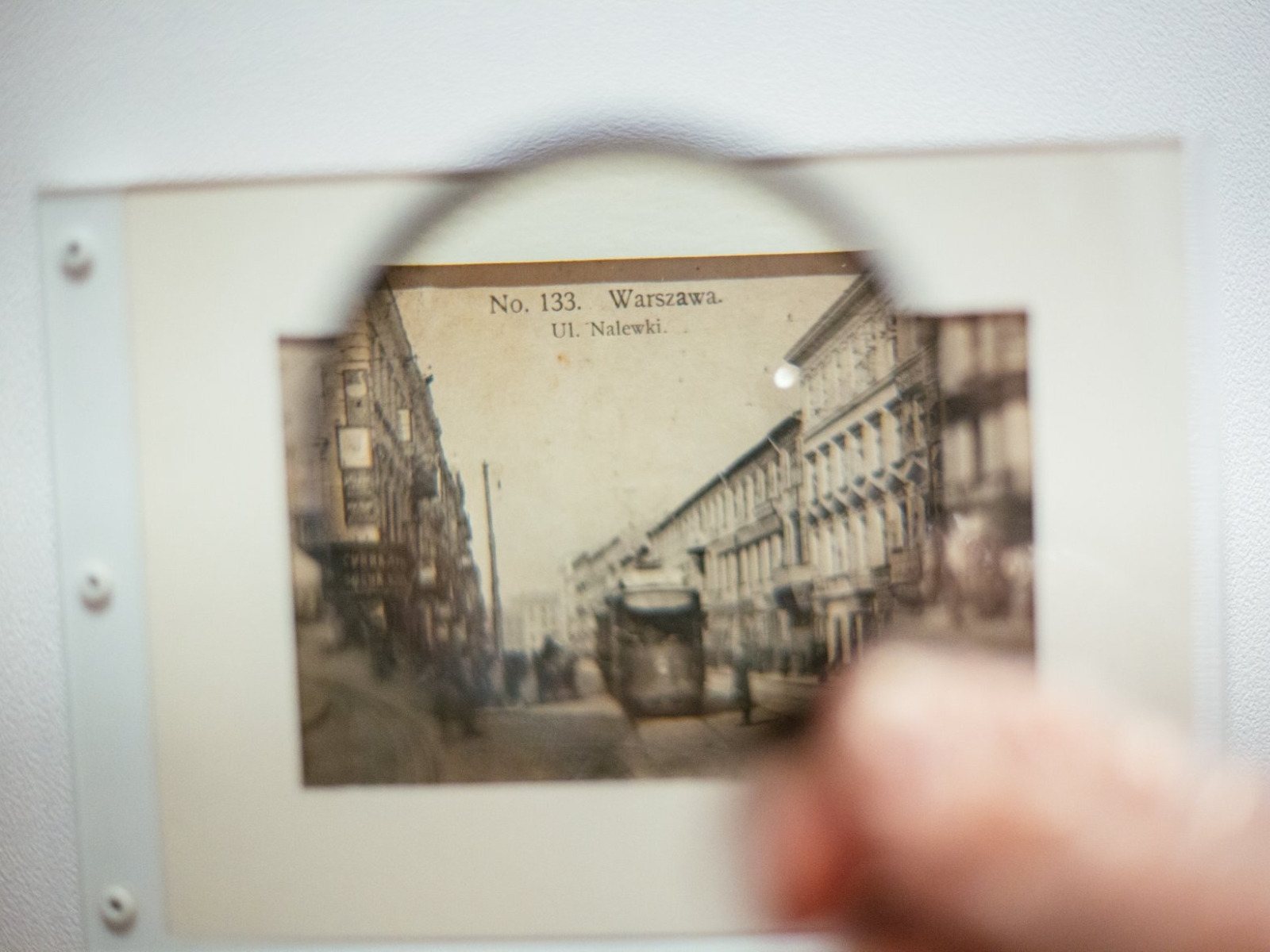 Ktoś przykłada lupę do zdjęcia archiwalnego warszawskiej ulicy Nalewki.