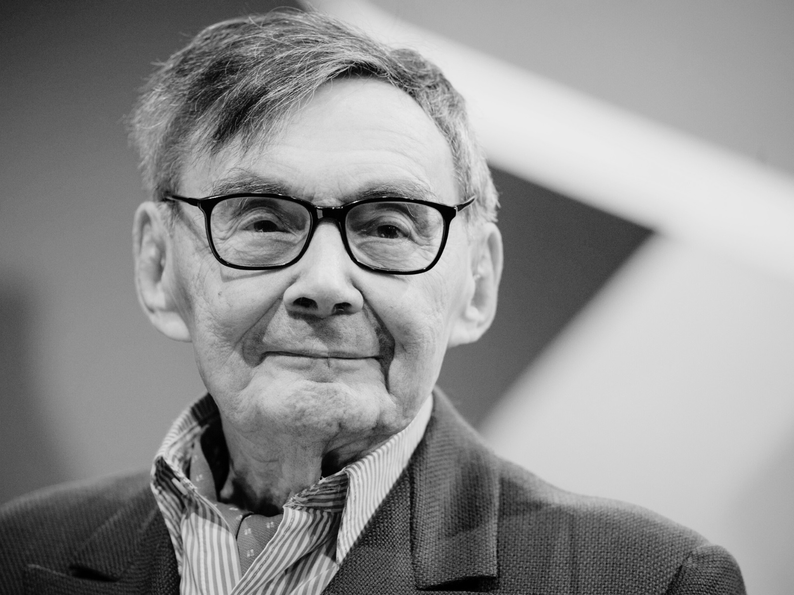 Uśmiechnięty Marian Turski. Zdjęcie w szarej tonacji.