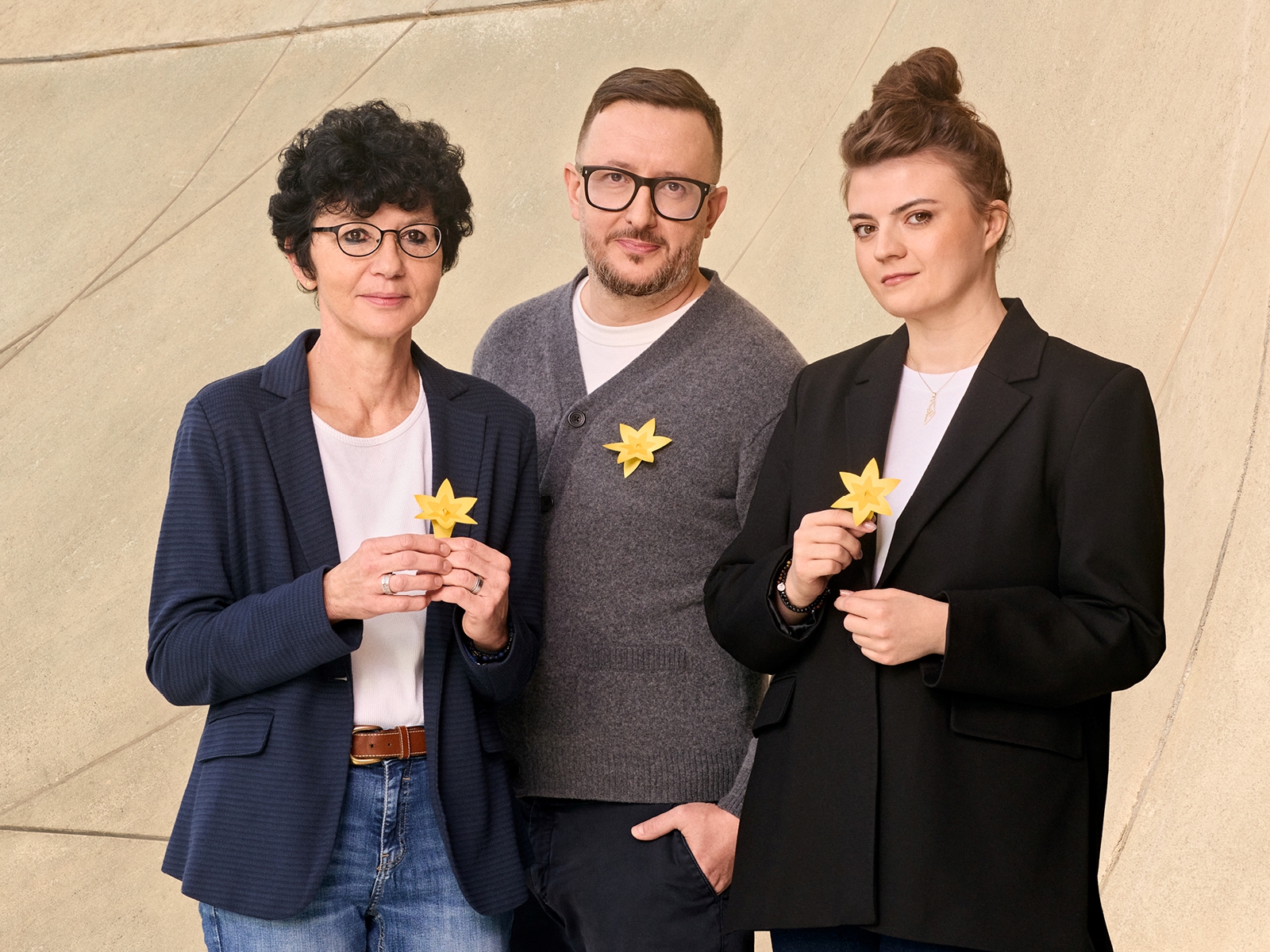 Dwie wolontariuszki akcji Żonkile trzymają papierowe kwiaty. Pośrodku stoi wolontariusz.