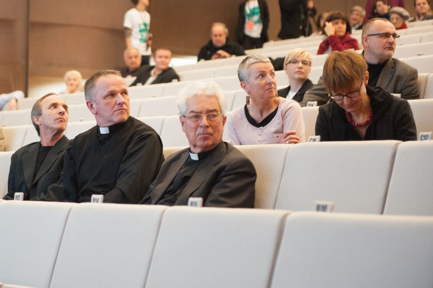 W audytorium siedzi kilka osób, w tym trzech księży.