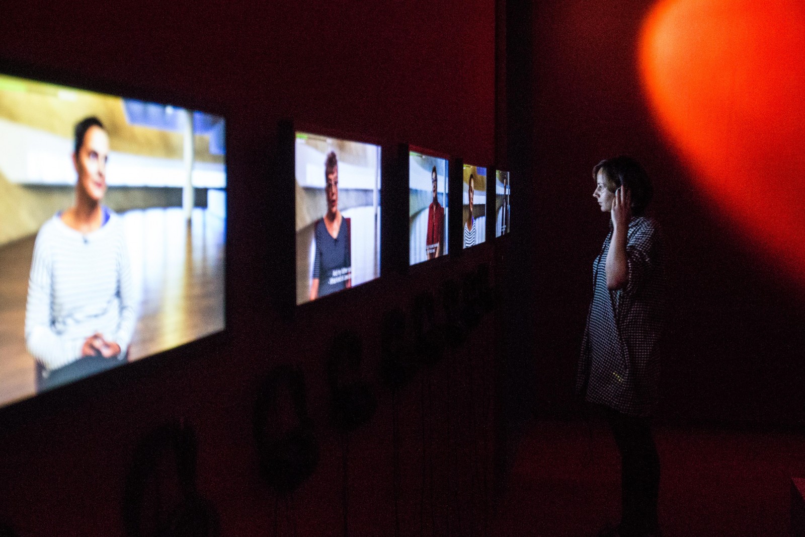 Dziewczyna stoi przed ekranami multimedialnymi, na których wyświetlają się sceny z filmu "Krew łączy i dzieli".
