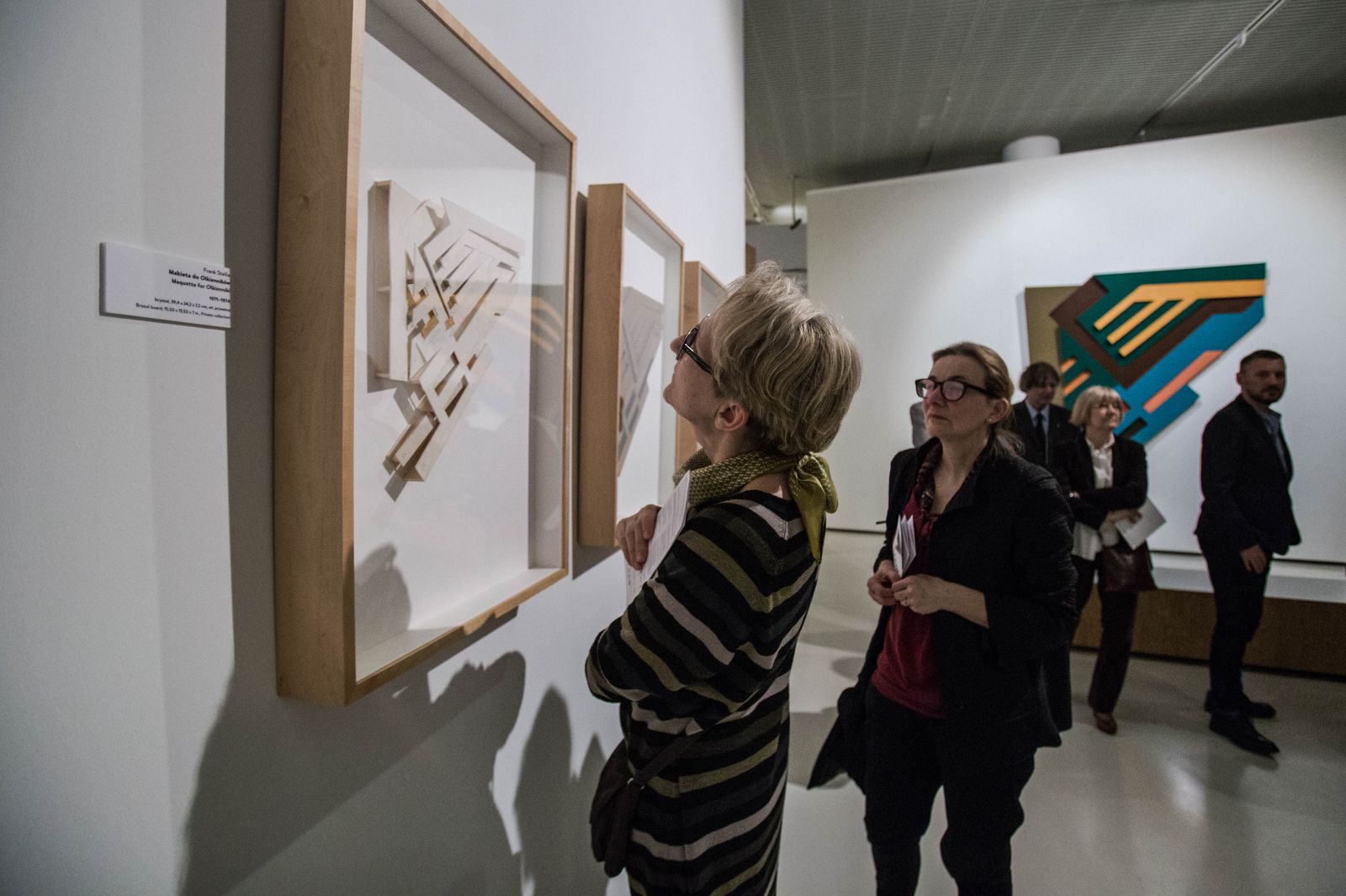 Sala w muzeum. Wystawa „Frank Stella i synagogi dawnej Polski”. Na pierwszym planie dwie kobiety oglądają obrazy. W tle grupa ludzi.  