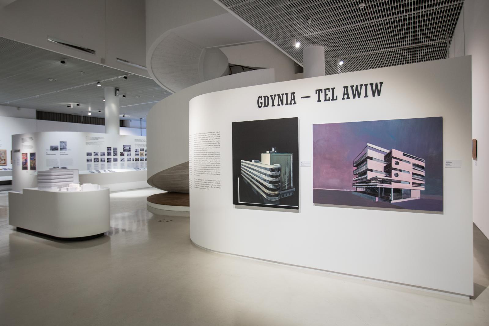 Wystawa czasowa "Gdynia - Tel Awiw" w Muzeum POLIN. Na zdjęciu dwa obrazy przedstawiające modernistyczne budynki wybudowane w Gdyni. Nad nimi napis - tytuł wystawy - Gdynia, Tel Awiw