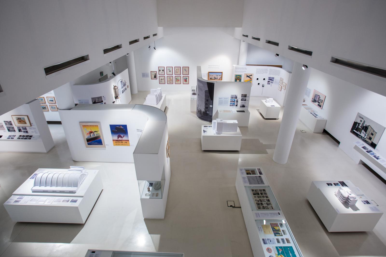 Wystawa czasowa "Gdynia - Tel Awiw" w Muzeum POLIN. Na zdjęciu widok wystawy z góry. Można oglądać białe ścianki działowe, gabloty z prezentowanymi przedmiotami, plakaty i obrazy