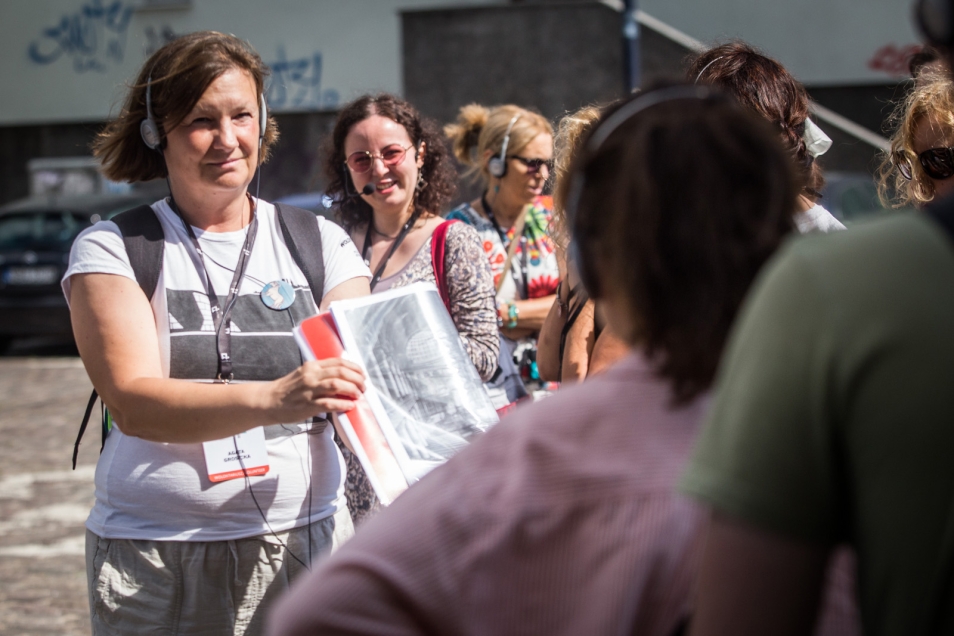 Na zdjęciu przewodniczka pokazuje zdjęcie grupie dorosłych osób, które oprowadza po mieście
