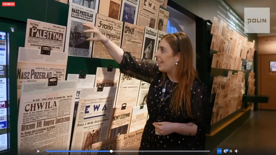Na zdjęciu kobieta (Katarzyna Jankowska) sięga do wystawionych na wystawie gazet z czasów przedwojennej Warszawy