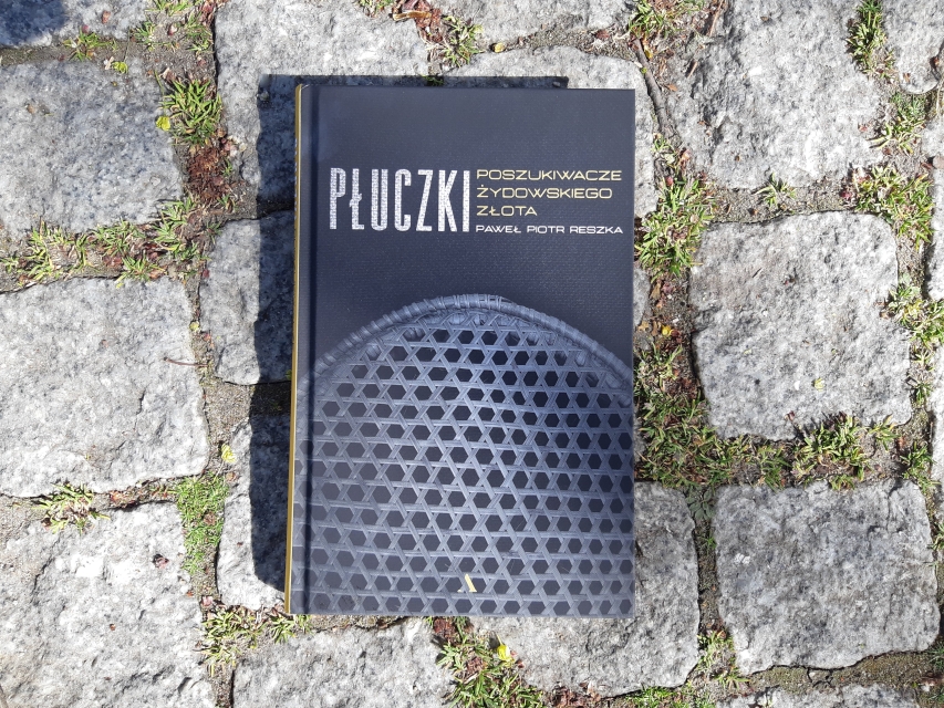 Okładka książki Paweł Piotr Reszka "Płuczki. Poszukiwacze żydowskiego złota". Książka leży na bruku ulicy