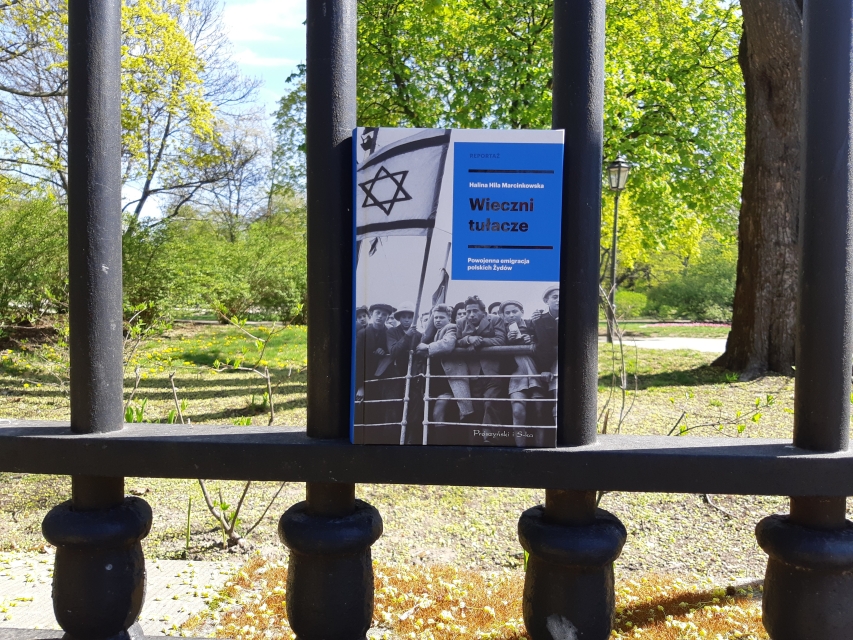 Okładka książki Halina Hila Marcinkowska "Wieczni tułacze. Powojenna emigracja polskich Żydów" - widać ją zza krat ogrodzenia