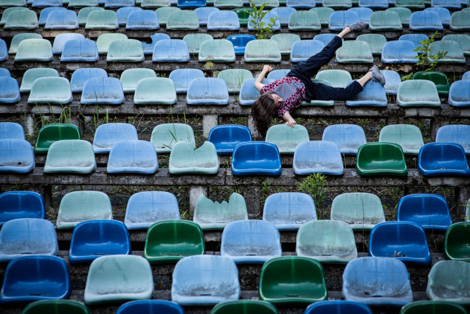 Na niebieskich stadionowych plastikowych krzesełkach leży jedna osoba, z głową w dół