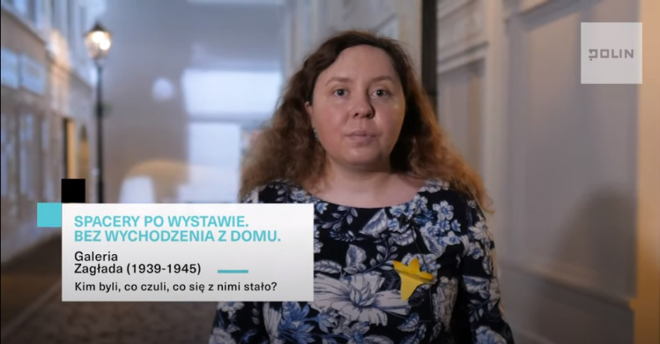 Kobieta w przestrzeni wystawy stałej Muzeum POLIN. Napis po lewej stroni: Spacery po wystawie. Bez wychodzenia z domu. Kim byli, co czuli, co się z nimi stało? Galeria Zagłada (1939-1945)
