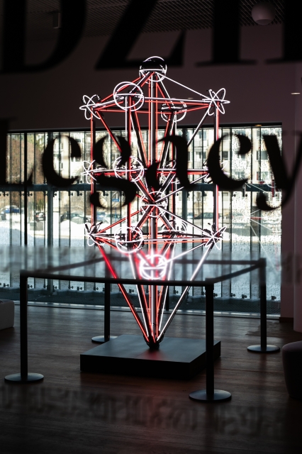 Widok na galerię Dziedzictwo przez szybę, na której jest napis Legacy. Wewnątrz widać rzeźbę Drzewo życia Huberta Czerepoka