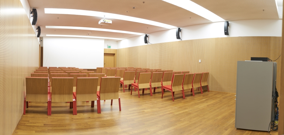 Pusta sala konferencyja - widok od drzwi wejściowych na ekran. Krzesła w rzędach widoczne od tyłu.