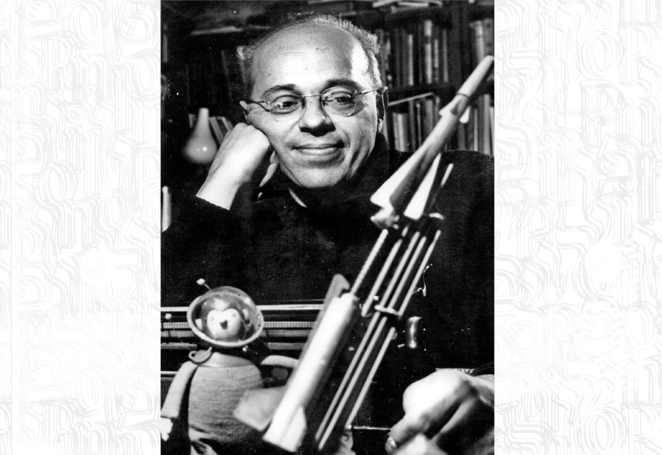 Mężczyzna w okularach (Stanisław Lem), w czarnym ubraniu. Podpiera policzek dłonią zamkniętą w pięść. Lekko się uśmiecha. Nosi okulary.