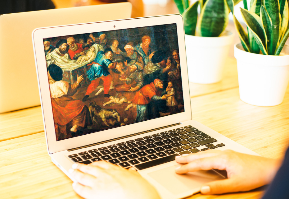 Otwarty laptop. Na ekranie wyświetla się obraz. W tle rośliny doniczkowe.