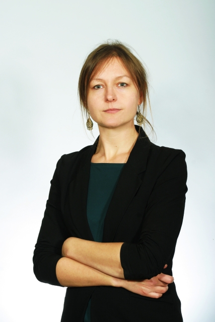 Lidia Zessin-Jurek. Kobieta w związanych włosach, z uszu zwisają jej kolczyki. Ubrana jest w czarną marynarkę i ciemną bluzkę. Stoi z założonymi rękami.