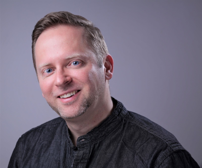 Michał Oleszczyk. Młody brunet o niebieskich oczach uśmiecha się do zdjęcia.