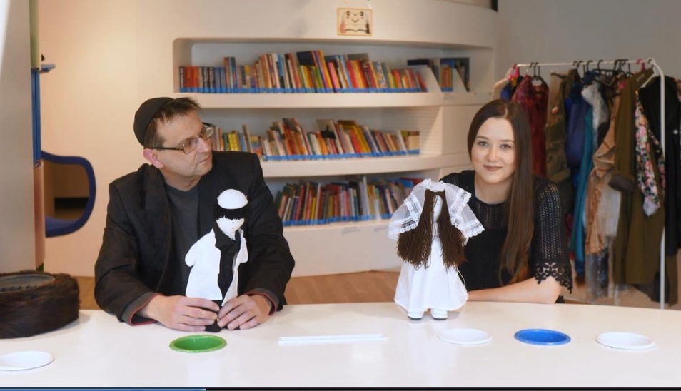 Kobieta i mężczyzna przedstawiają małe modele ubrane w żydowskie stroje ślubne - męski i damski.