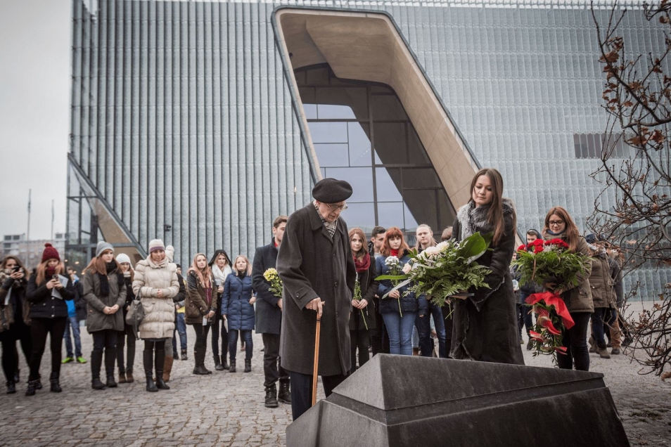 Władysław Bartoszewski z młodzieżą przed pomnikiem Rady Pomocy Żydom "Żegota". W tle budynek Muzeum POLIN.