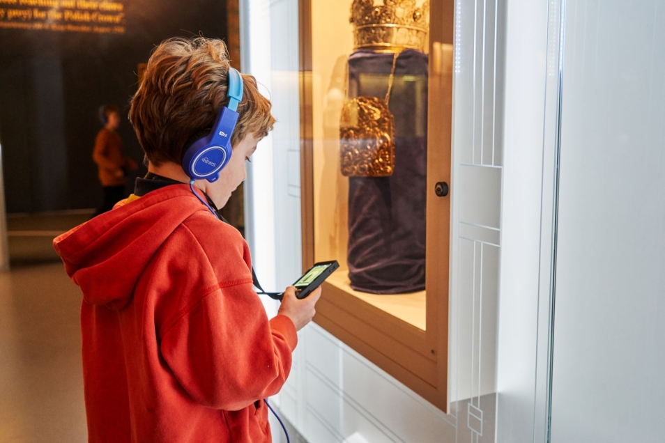 Chłopiec w niebieskich słuchawkach odtwarza treści z audioprzewodnika na wystawie stałej w Muzeum POLIN.