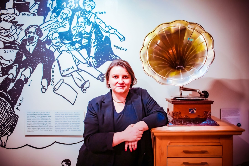 Agnieszka Kuś - przewodniczka Muzeum POLIN - stoi przy gramofonie na wystawie stałej.