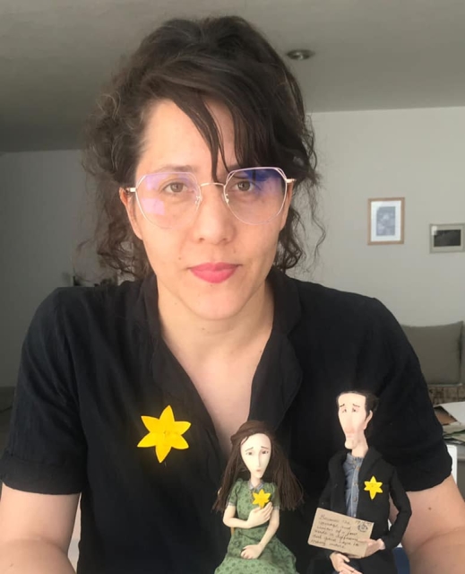 A girl from Mexico with two puppets. All of them wear paper daffodils on their clothes.