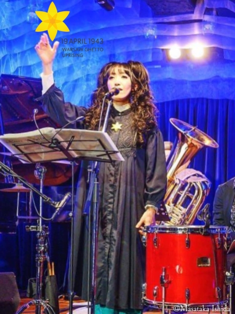 The 78. anniversary of the outbreak of the Warsaw Ghetto Uprising. On a music stage there is a Japanese girl. She is singing some song connected with anniversary.