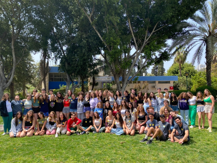 Sunny day in Israel. A group of students standing or sitting on a grass in front of a school. They are wearing paper daffodils on their clothes.