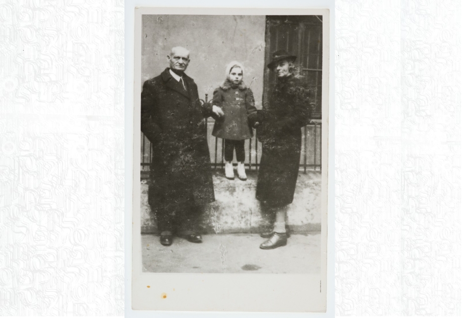 Mała Aleksandra Rozengarten (obecnie Kaniuka) stoi na ogrodzeniu. Za ręce trzymają ją matka Irena i dziadek Eliezer Rozengarten. / Aleksandra Rozengarten is standing on a fence, her mother Irena and grandfather Eliezer Rozengarten holding her hands.